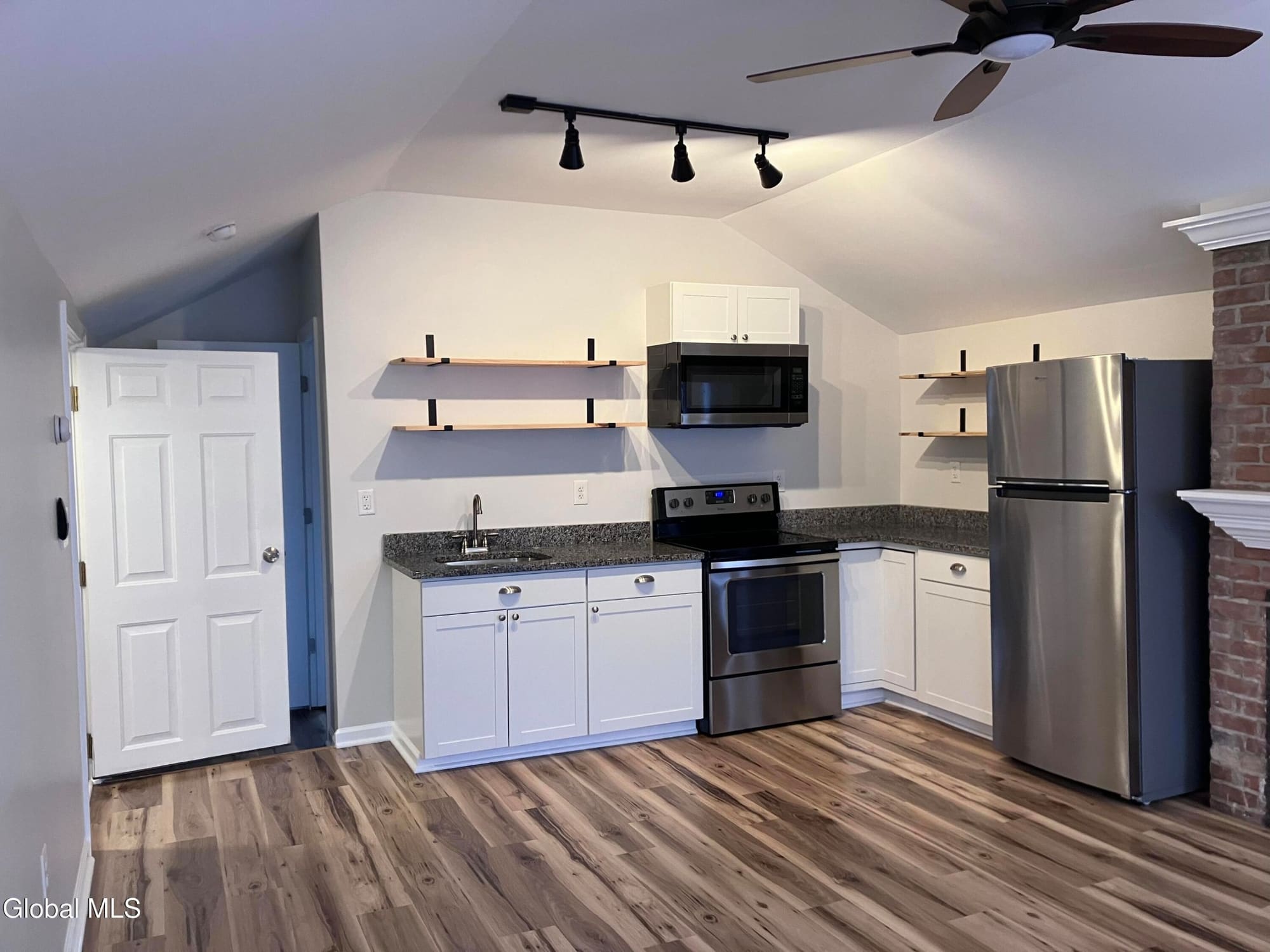 Modern kitchen with white cabinets, stainless steel appliances, and floating shelves