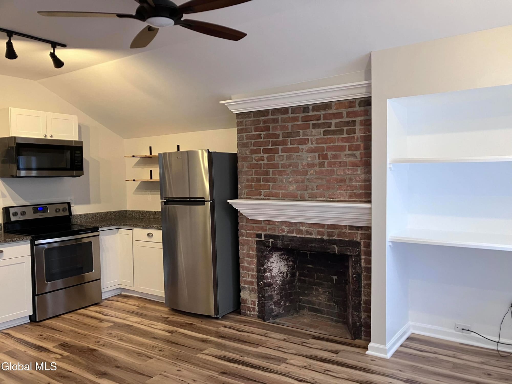 Modern kitchen with stainless steel appliances, white cabinets, granite countertop, and exposed brick fireplace