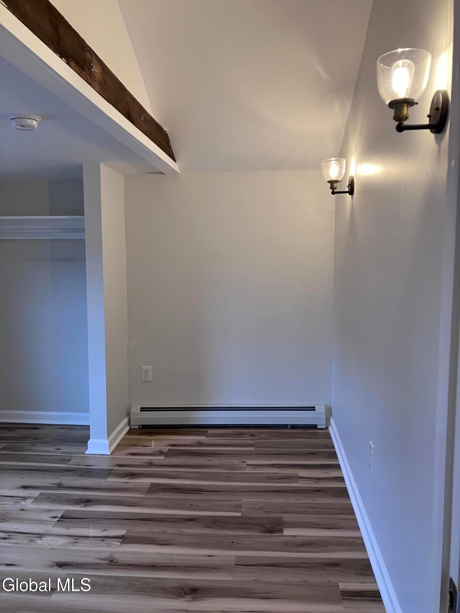 Modern empty room with wood flooring, white walls, exposed beam, and wall sconces