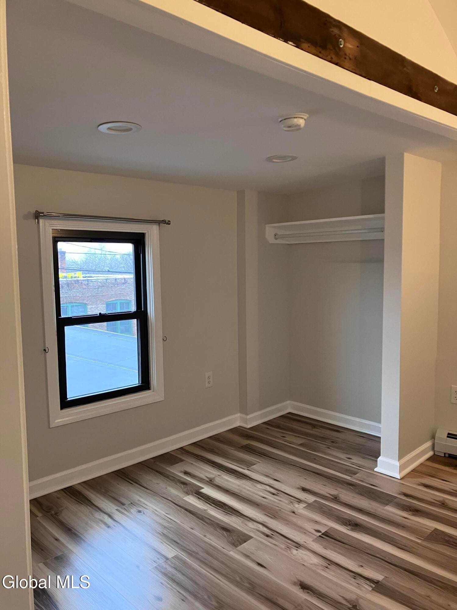 Modern bedroom with hardwood floors, window, and built-in closet with rod