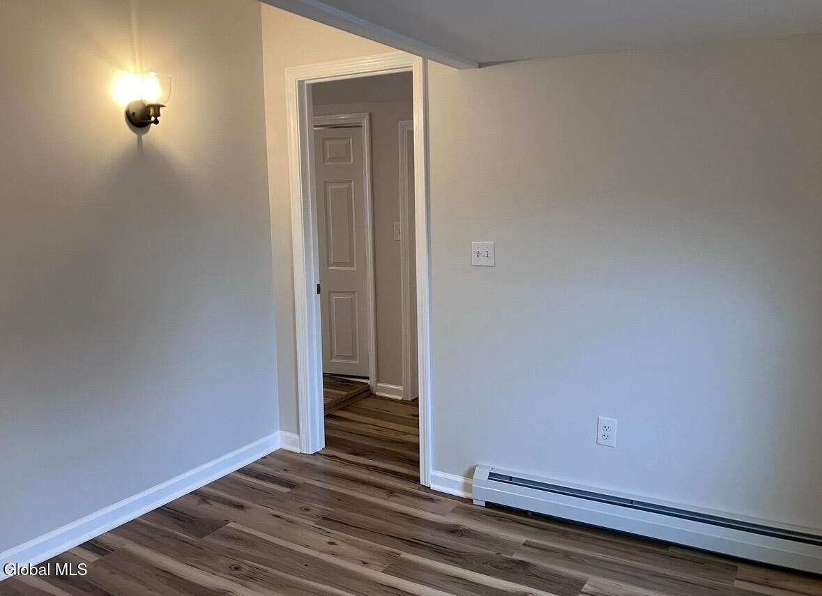 Empty room with wood flooring, white walls, wall sconce, electrical outlets, and open doorway