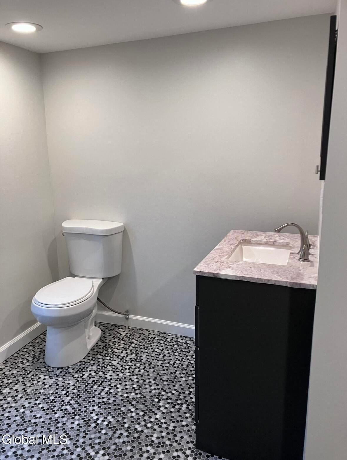Modern bathroom with white toilet, black vanity with marble countertop, and speckled tile flooring