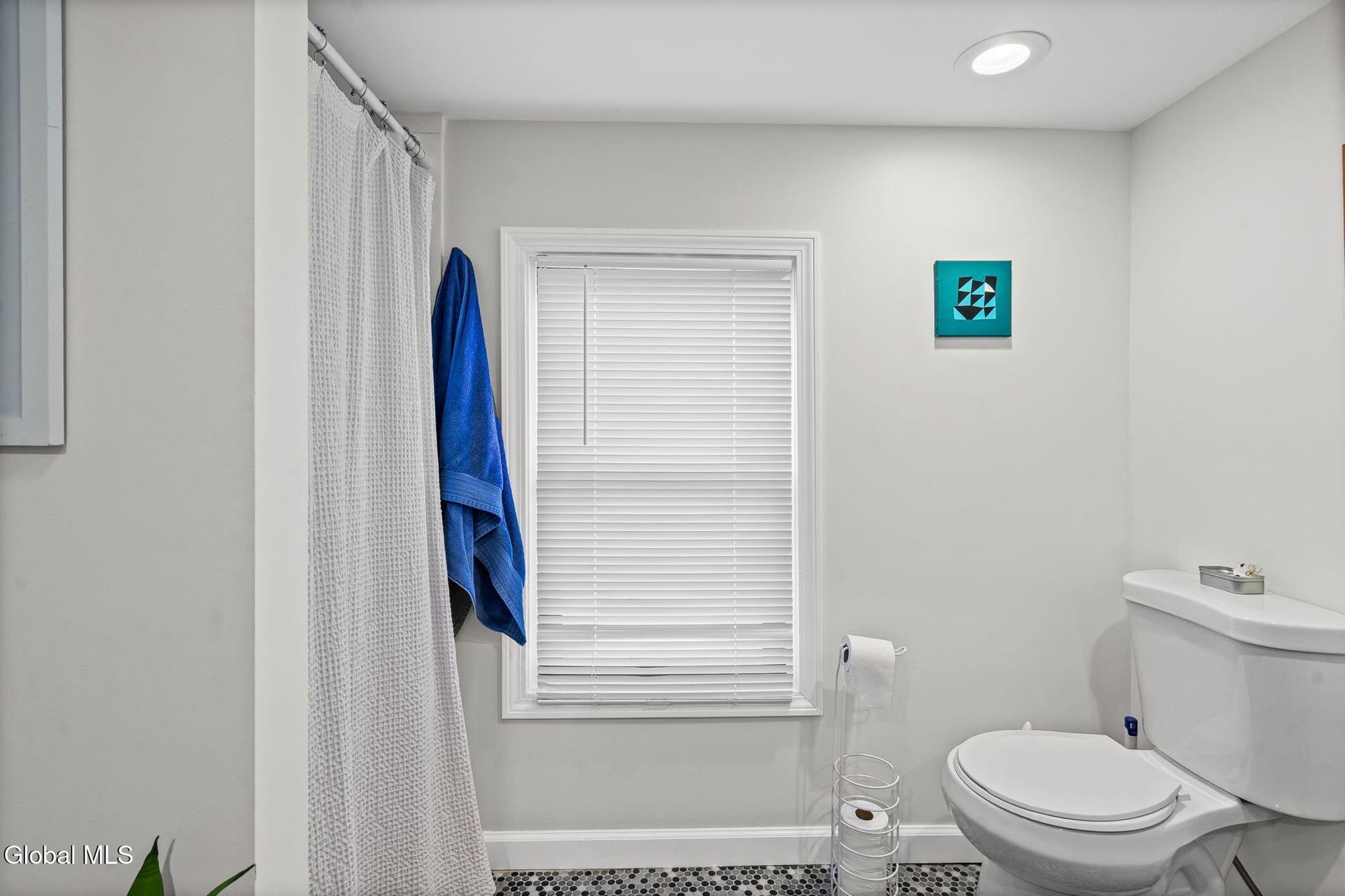Modern bathroom with white walls, toilet, sink, shower with curtain and window blinds
