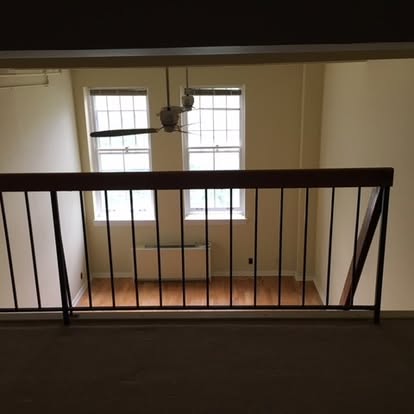 Black metal railing on loft overlooking cream-colored room with windows