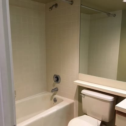 Clean bathroom with white tile walls, bathtub, toilet, and mirror above sink
