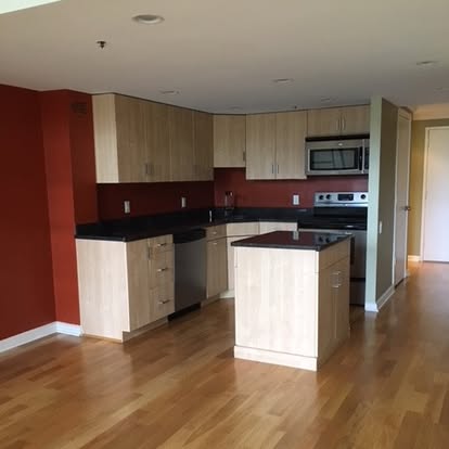 Modern kitchen with white cabinetry, red accent wall, black countertops, and central island
