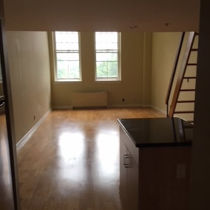 Empty loft space with hardwood floors, two windows, and staircase