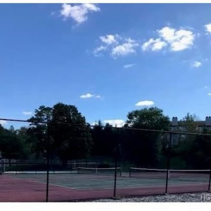 Outdoor tennis courts with red clay surface surrounded by black fencing on clear sunny day
