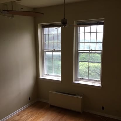 Empty room with two large windows, wooden floor, and radiator heater below windows