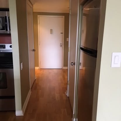 Hallway with hardwood floors, white walls, and multiple doorways leading to kitchen and other rooms