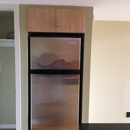 Stainless steel refrigerator built into kitchen cabinetry with wood cabinets above
