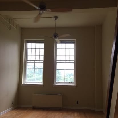 Empty room with two tall windows, ceiling fan, and hardwood flooring