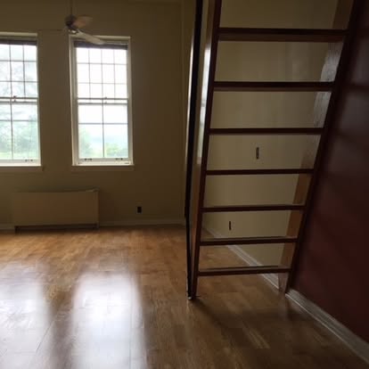 Empty room with hardwood floors, large windows, and dark wooden shelving unit