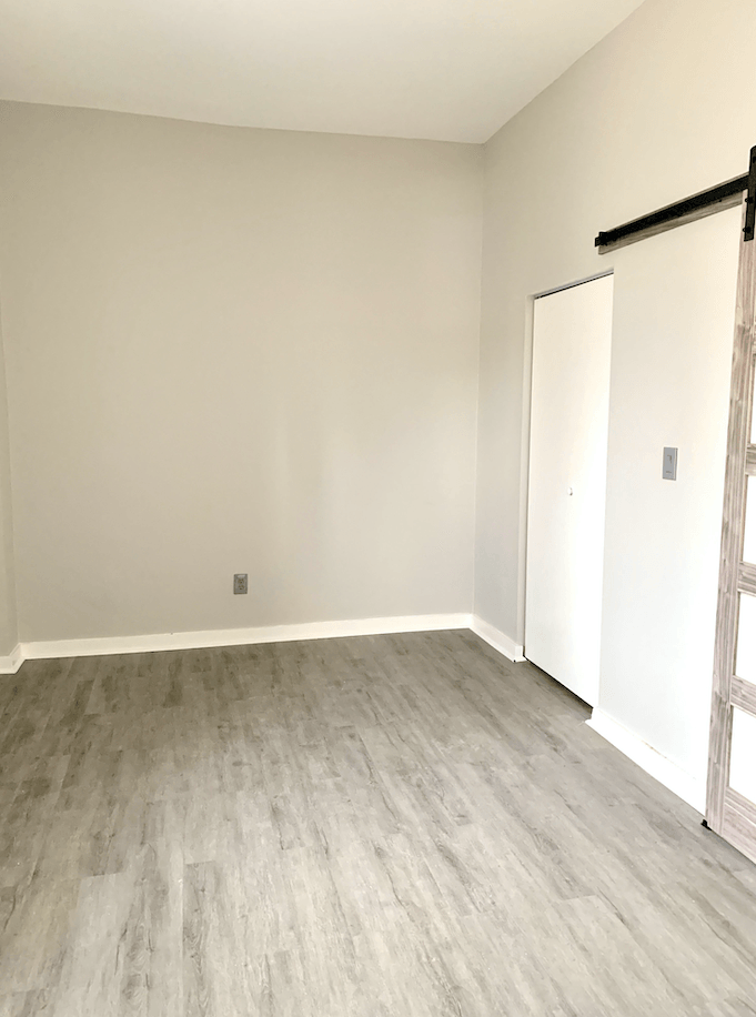Empty bedroom with gray wood-look flooring, white walls, and white closet doors