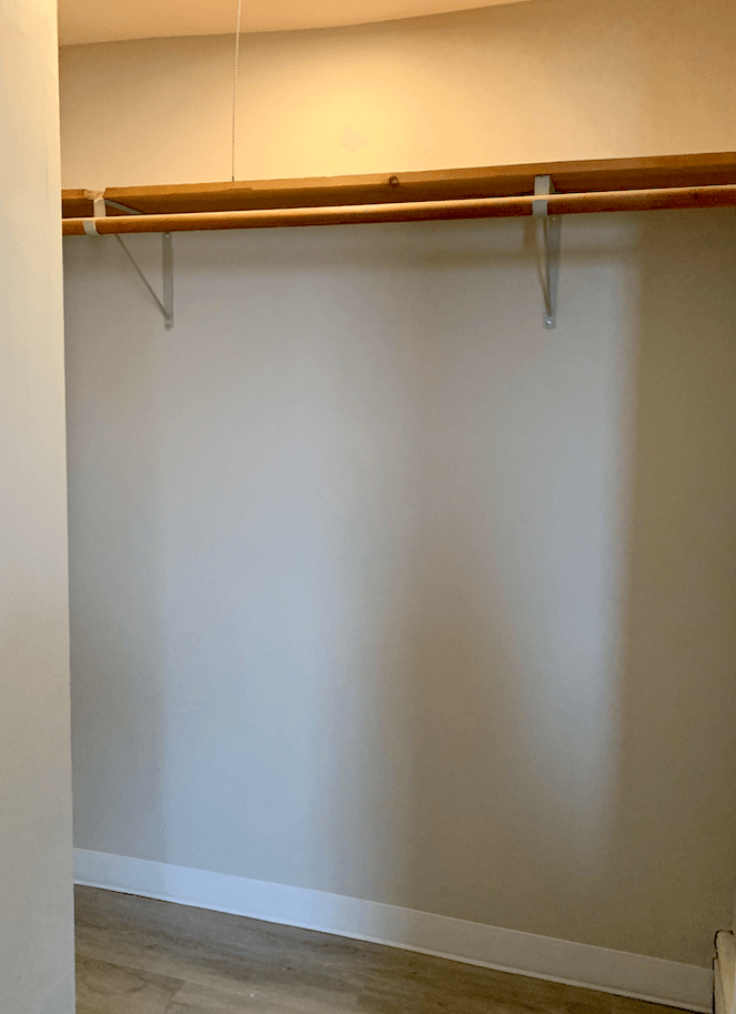 Empty closet with wooden rod mounted on metal brackets above hardwood floor