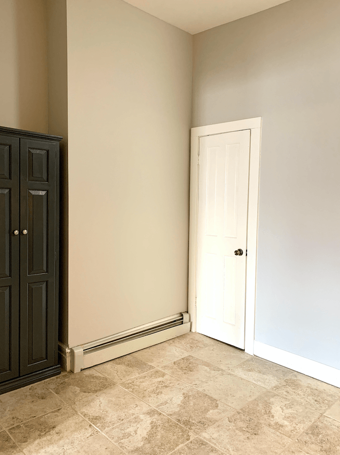 Empty room with beige walls, tile flooring, dark wooden wardrobe, white door, and baseboard heater