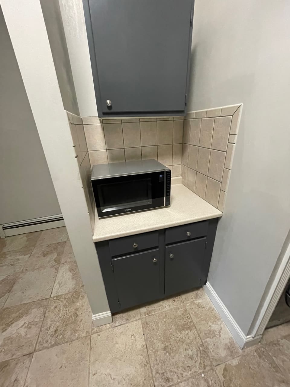 Microwave oven mounted above black cabinet with beige tile backsplash in kitchen alcove