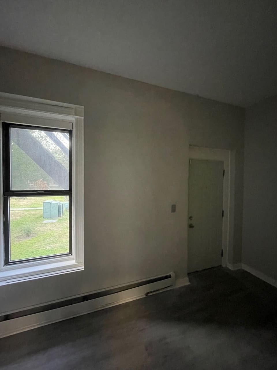 Empty room with double-hung window overlooking lawn and baseboard heating