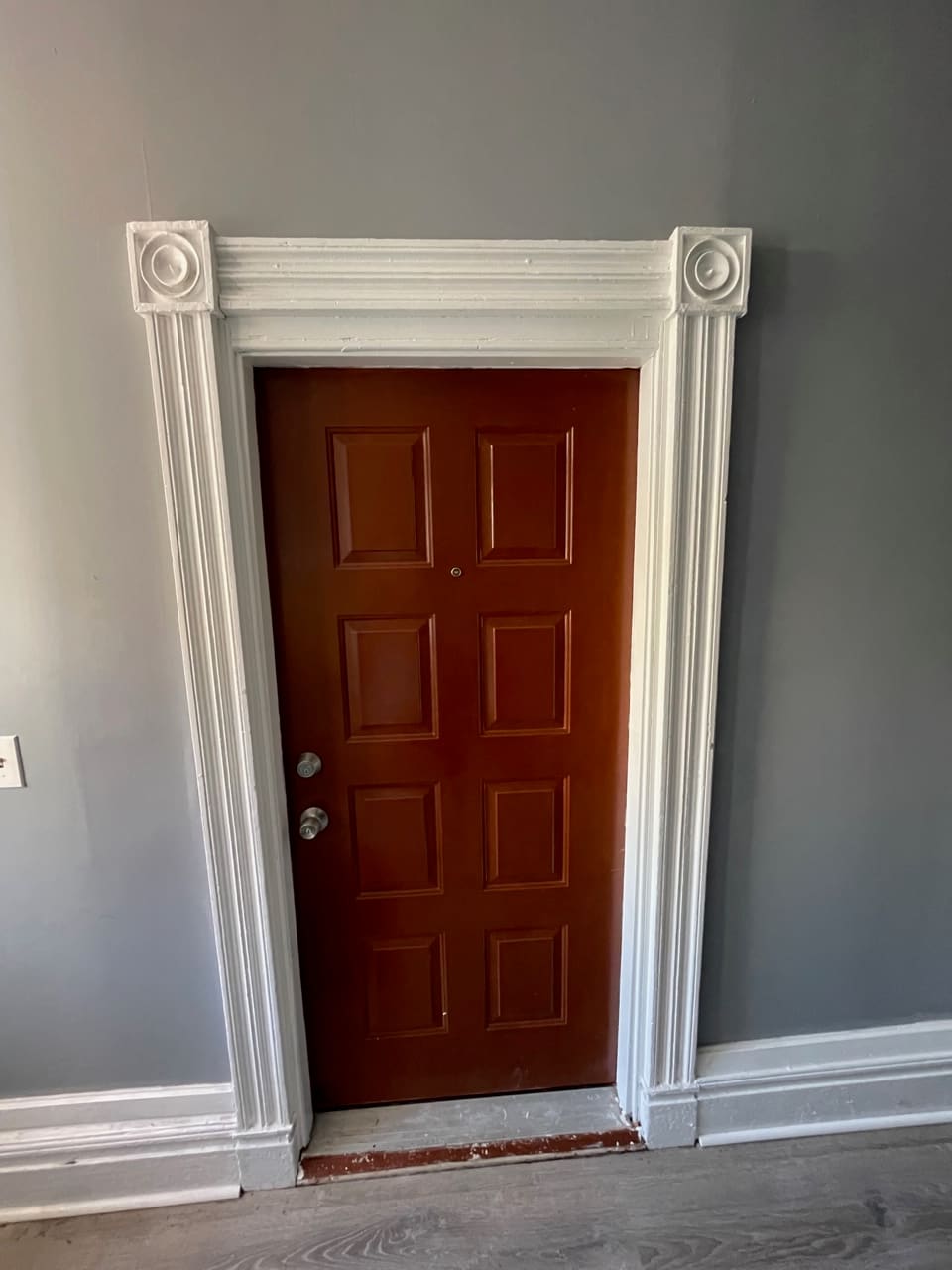 Red six-panel door with white ornate trim and rosette corner blocks