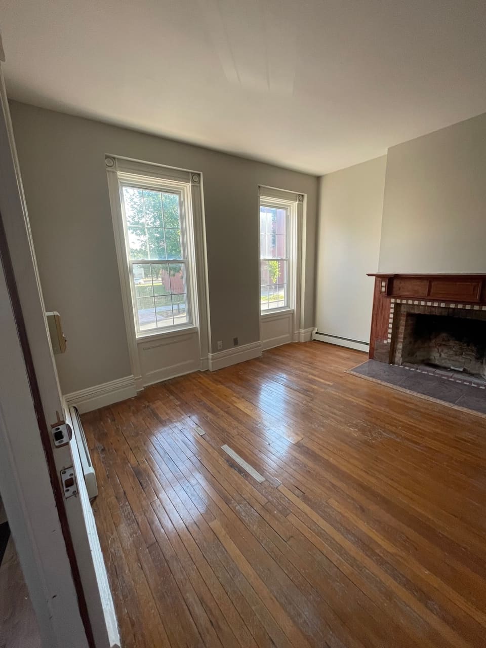 Empty living room with hardwood floors, fireplace, and dual windows with white trim
