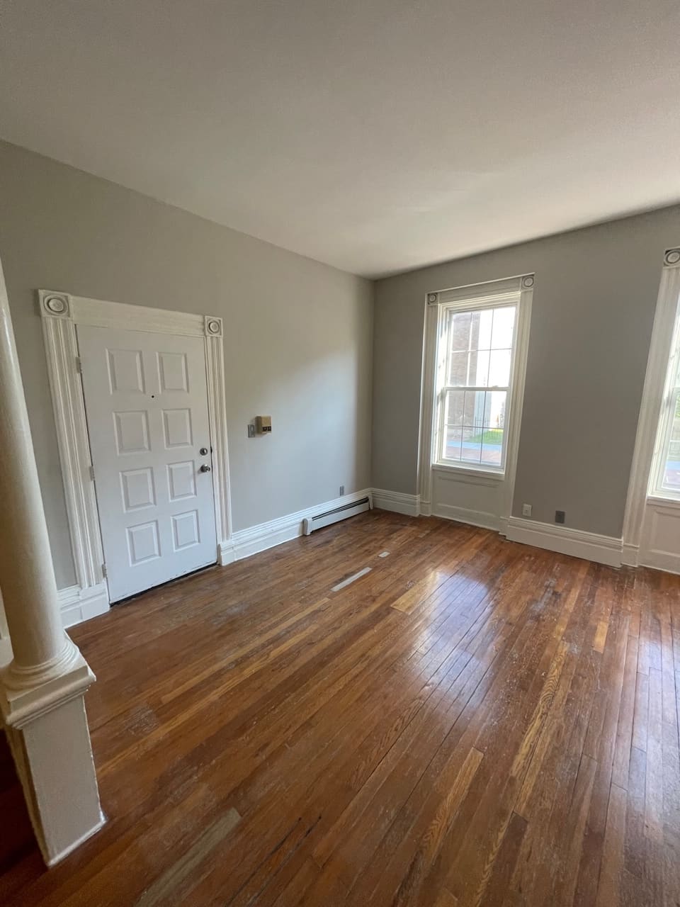 Empty room with hardwood floors, white trim door, two windows, and gray walls