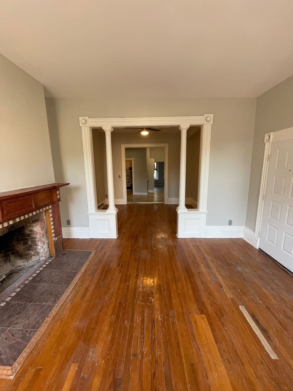 Spacious living room with hardwood floors, fireplace, white columns, and doorway to additional rooms