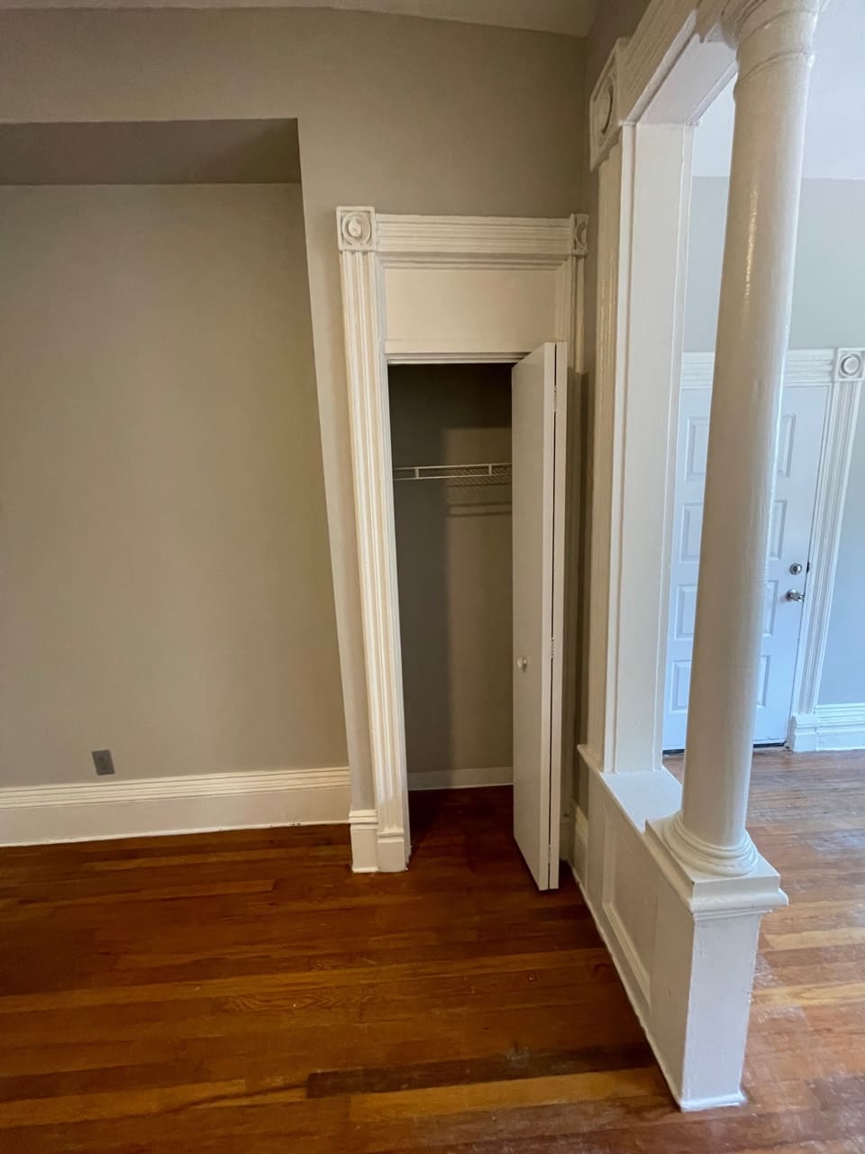 Empty room with hardwood floors, cream walls, white trim, support column, and open closet door