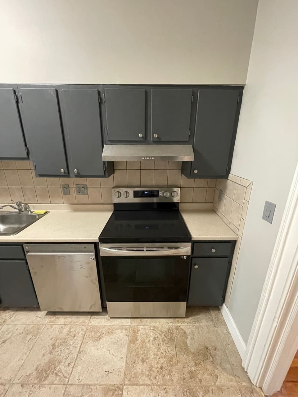 Modern kitchen with stainless steel appliances, dark cabinets, and beige tile backsplash