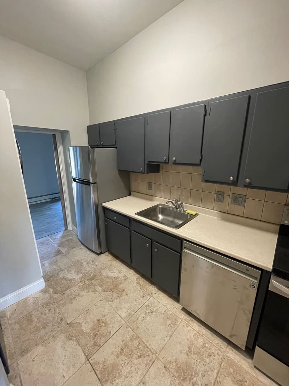 Kitchen with stainless steel appliances, dark cabinets, beige countertop and tile flooring
