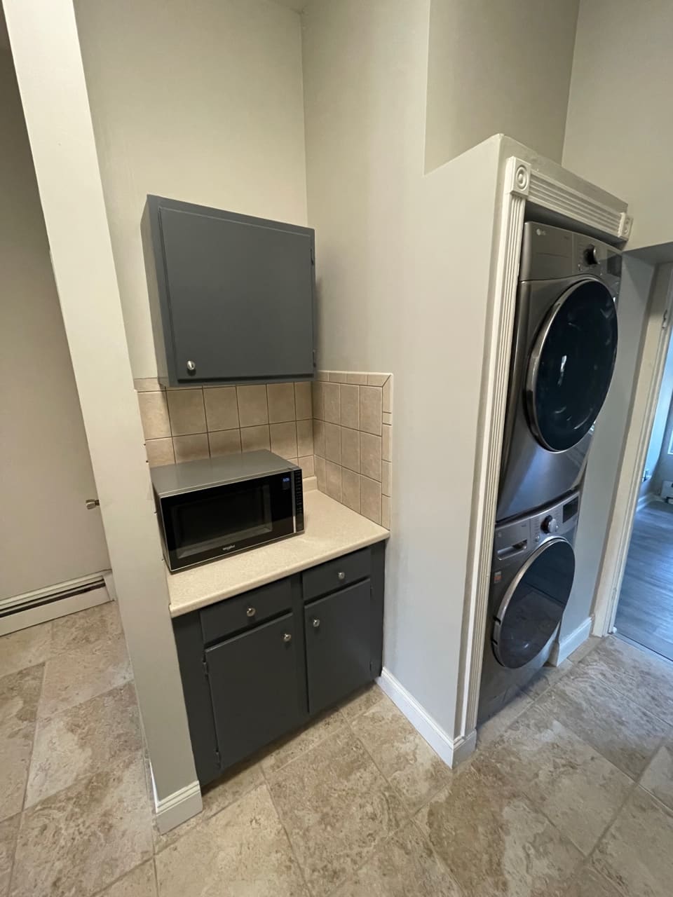 Modern laundry room with stacked washer and dryer, microwave, and cabinet storage