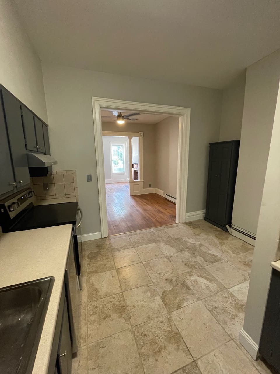 Kitchen with tile flooring, black appliances, and doorway leading to living room with hardwood floors