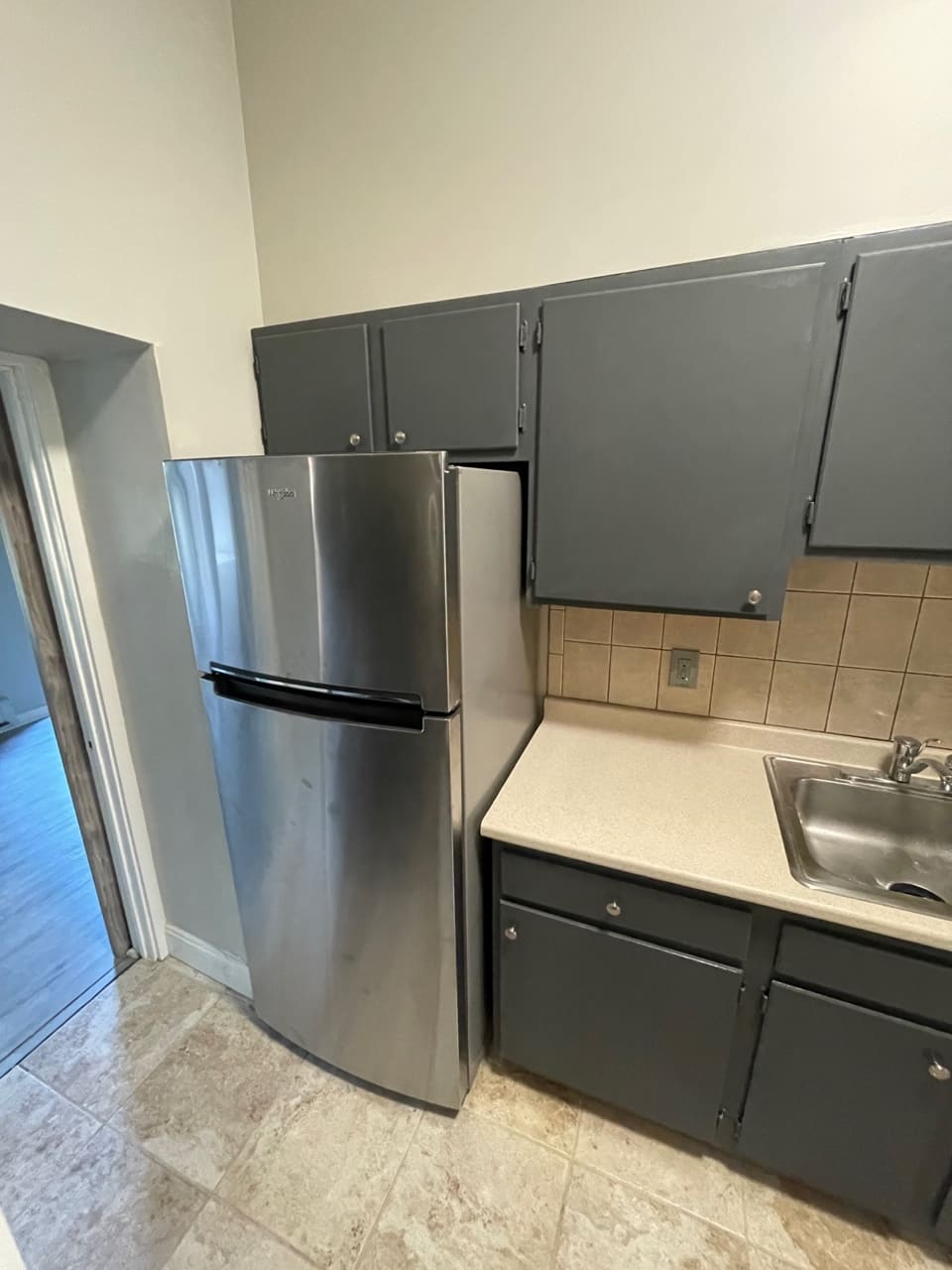Modern kitchen with stainless steel refrigerator, gray cabinets, and beige countertop with sink