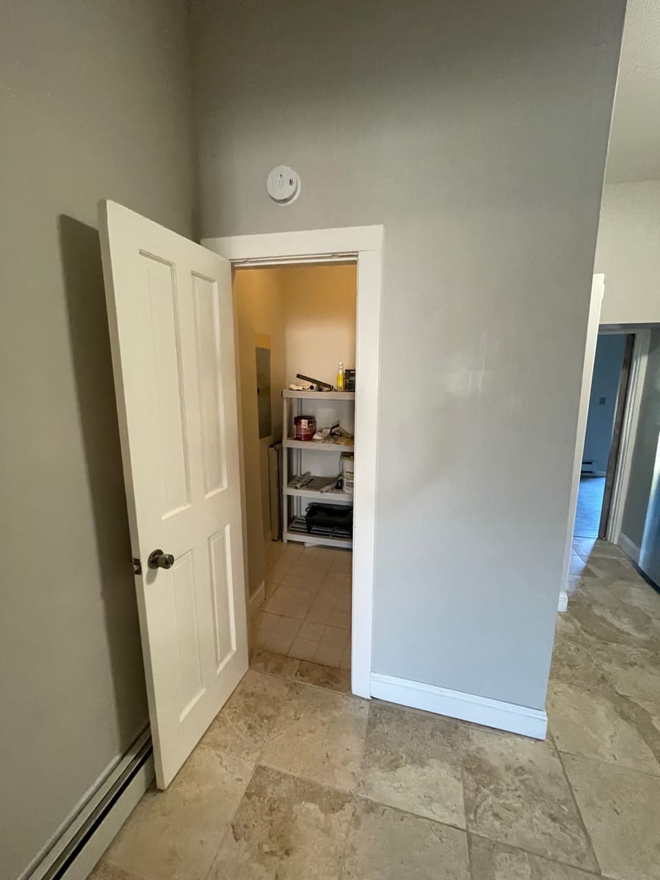 Open pantry closet with white doors and shelving inside a kitchen hallway