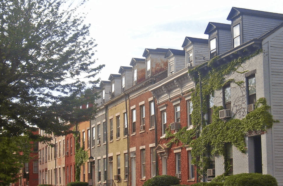 Row of historic townhouses with mansard roofs and ivy-covered facades along a tree-lined street